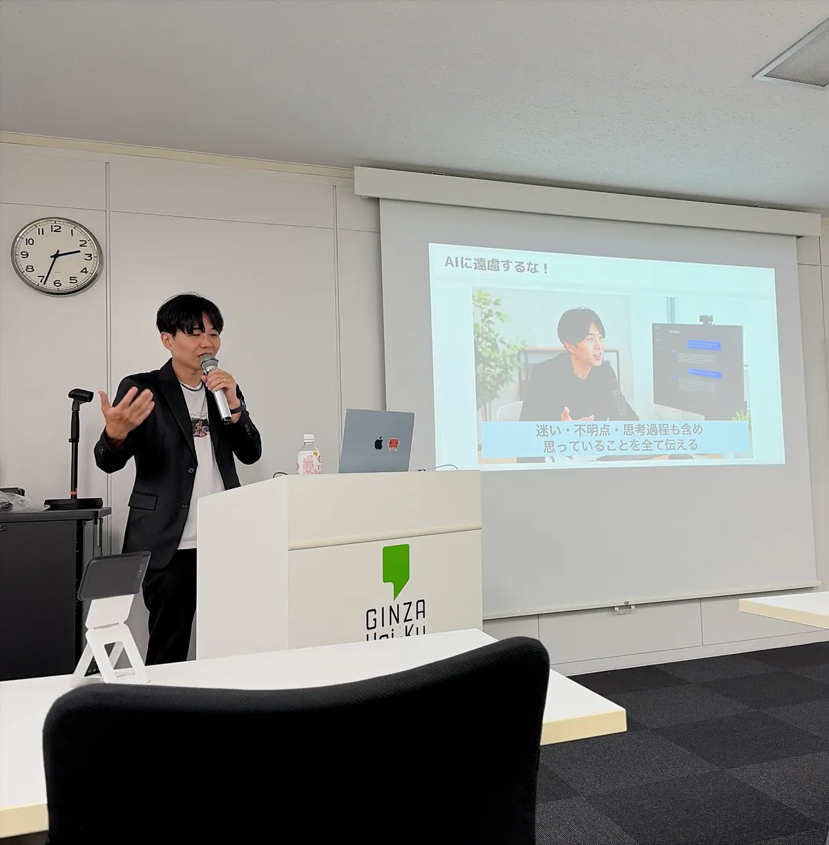 登壇中のみやっち🧑‍💻がマイクを持って話している。スクリーンのスライド見出しは「AIに遠慮するな！」、映像のキャプションに「迷い・不明点・思考過程も含め 思っていることを全て伝える」と表示されている