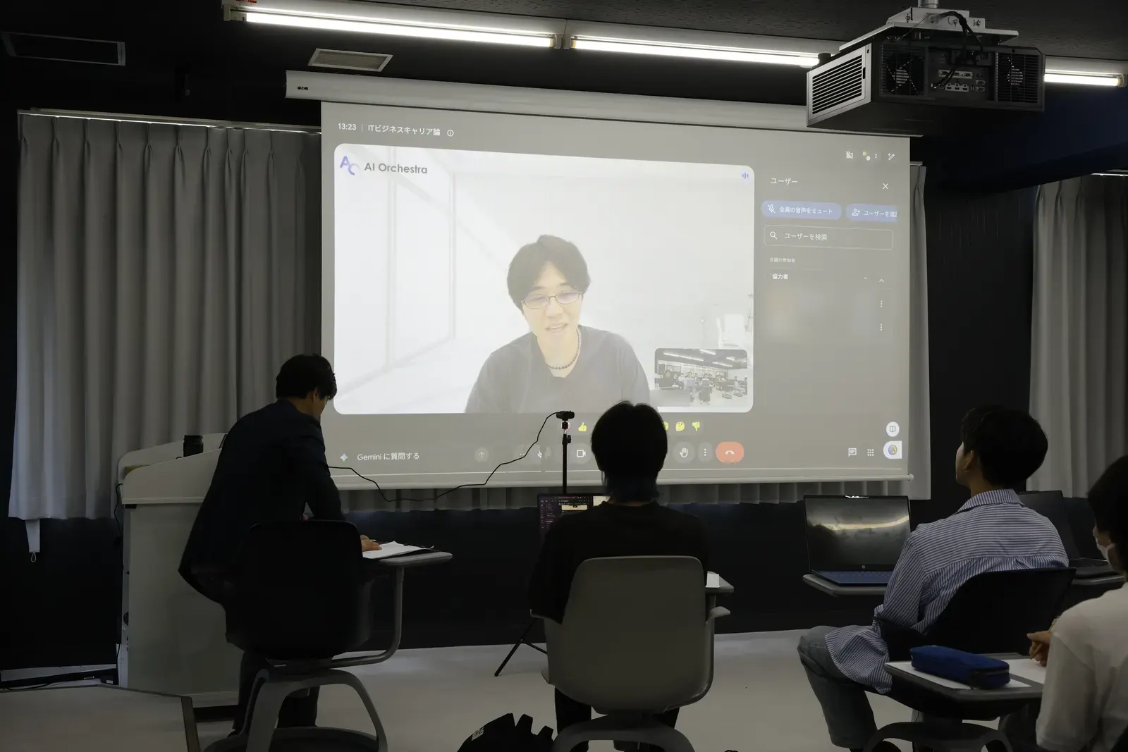 教室のスクリーンに映し出された宮地俊充がオンラインで講演する様子。学生たちがスクリーンに向かって聴講している