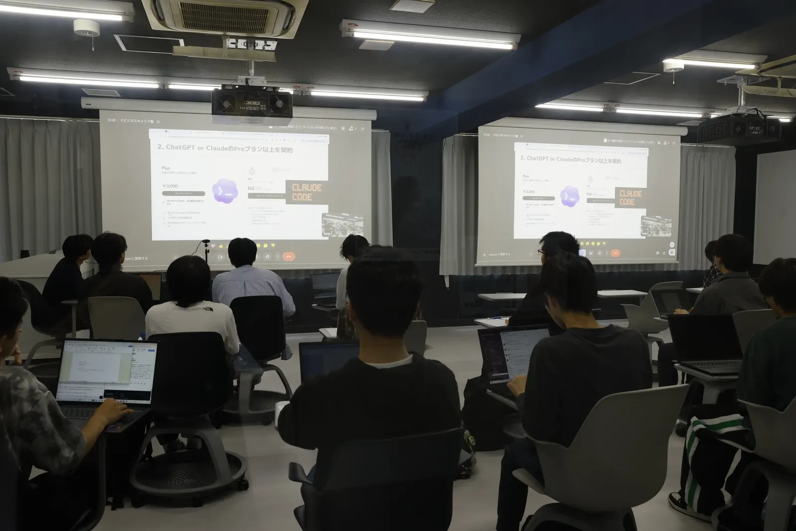 「ChatGPT or ClaudeのProプラン以上を契約」というスライドが映し出された教室で、ノートPCを開いて聴講する学生たち