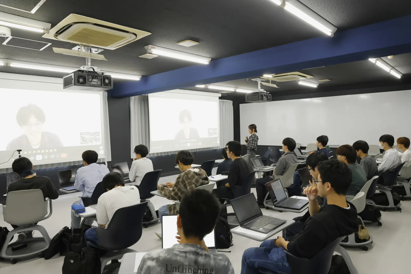 マイクを手に立って質問する学生と、スクリーンに映る宮地。質疑応答の様子